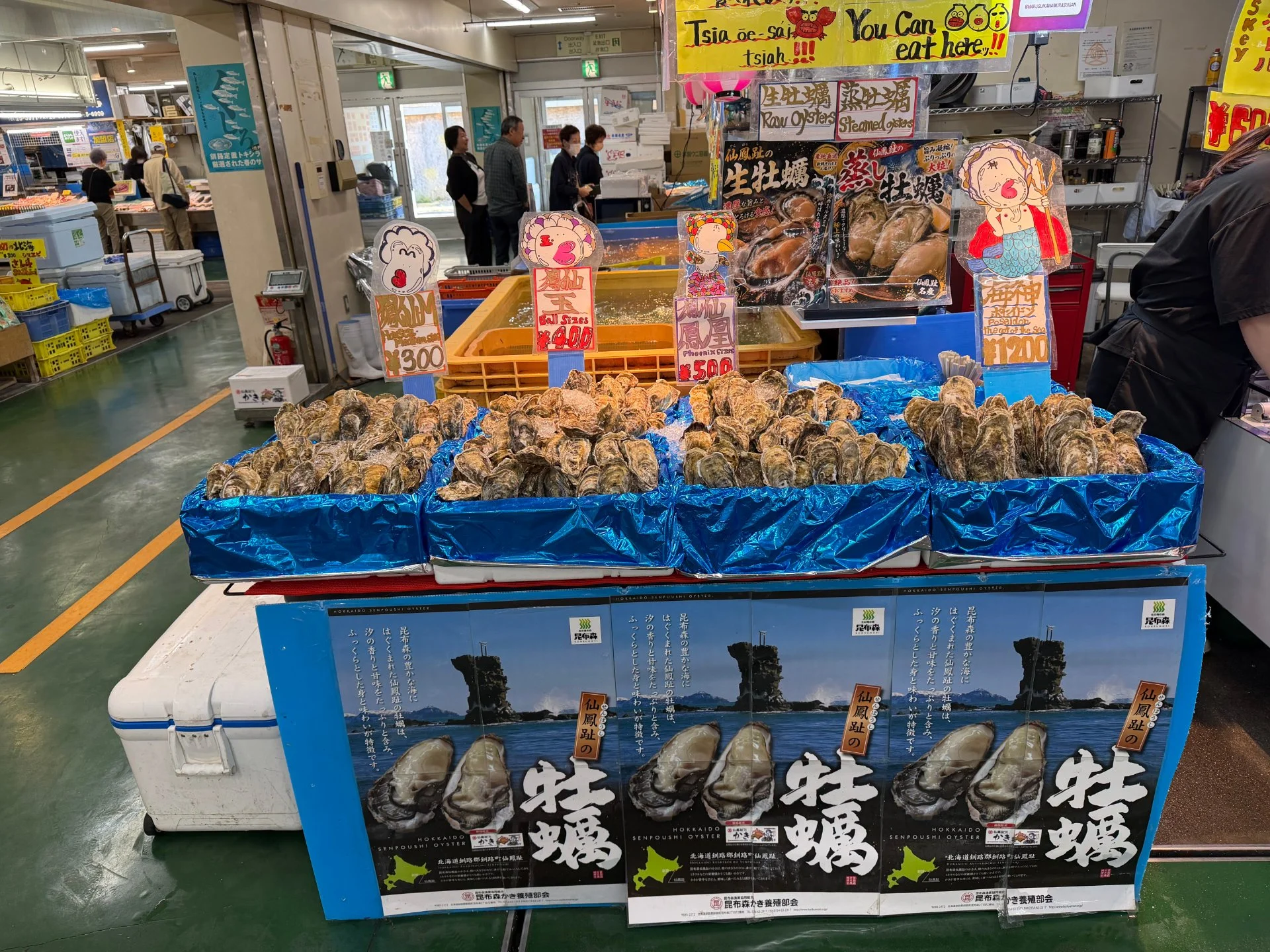 牡蠣の陳列と海鮮を紹介するポスターが並ぶ市場の売り場